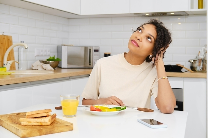 Cute african american woman daydreaming at breakfast in the kitchen