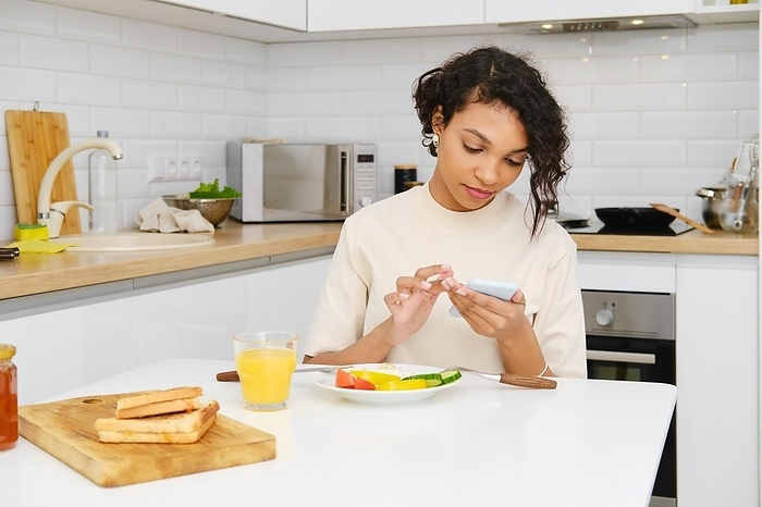 Young african woman reading message on mobile while having breakfast in the morning