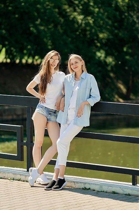 Two cheerful student girls standing on the bridge in hot sunny day