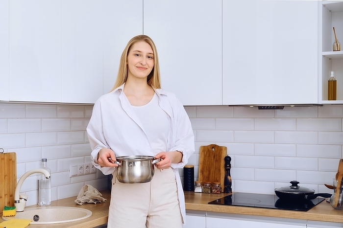 Young woman holds saucepan in hands, she is going to put it on the stove to boil