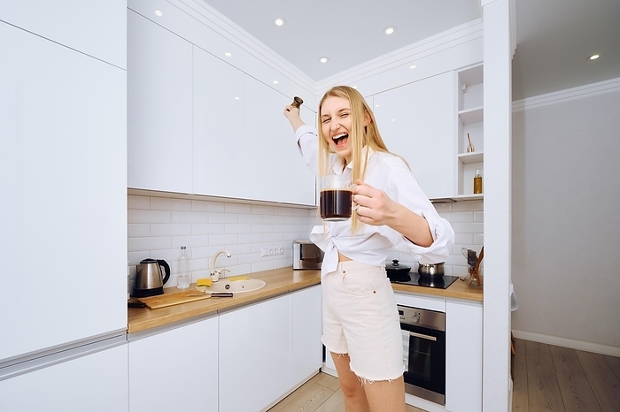 A heerful woman dancing and singing with a cup of coffee in hand in the kitchen
