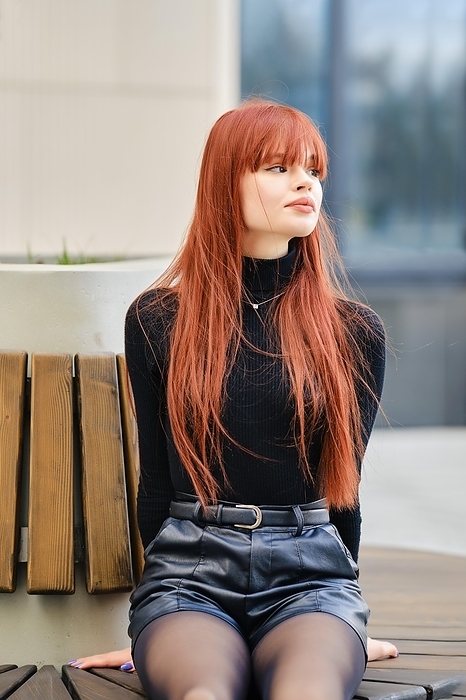 Young redhead woman sits patiently on bench and looking away