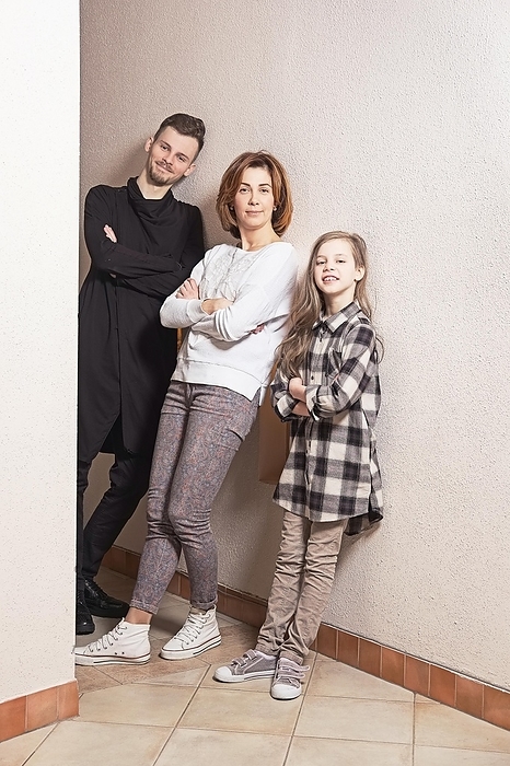 Cheerful family with crossed hands leaning against the wall at home