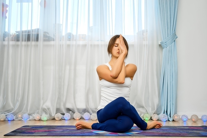 Young woman practicing yoga at home, sits with intertwined hands