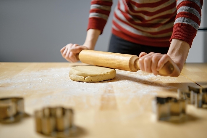Unrecognizable woman rolls out ginger dough with rolling pin on kitchen table (selective focus photo)