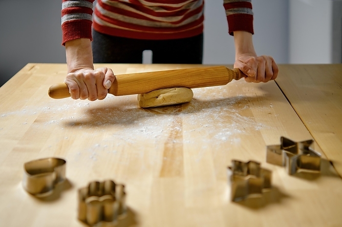 Unrecognizable woman rolls out ginger dough with rolling pin on kitchen table