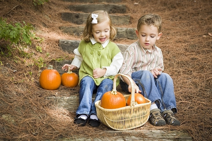 Cute young brother and sister children sitting on wood steps laughing with pumpkins in a basket