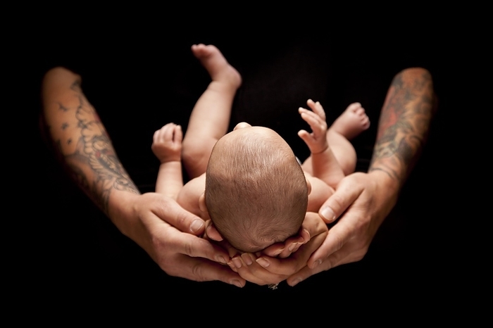 Hands of father and mother hold newborn baby under dramatic lighting against A black background