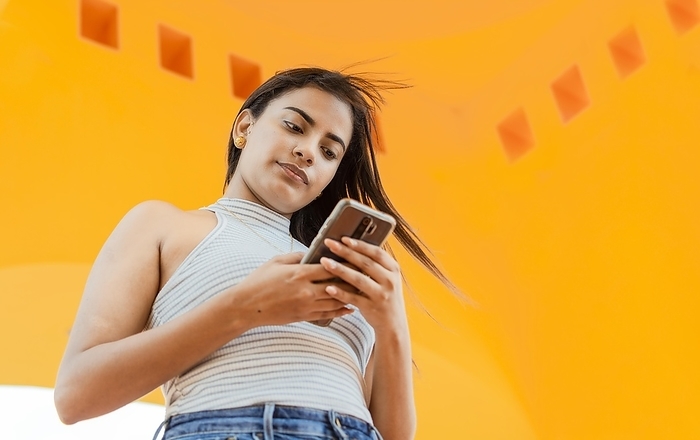 Portrait of attractive latin girl messaging on cell phone. Low angle of a beautiful Latin girl using the smart phone. Low angle of a young latin woman texting on cell phone