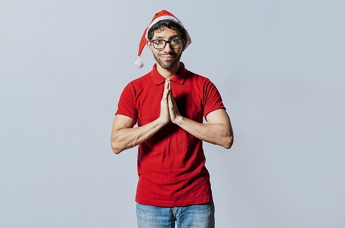 Man in christmas hat with hands together making a wish isolated. Guy with hands together making a christmas wish, Concept of christmas hat person making a wish