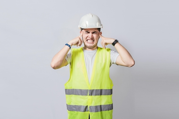 Young engineer covering his ears isolated, Builder man with ear pain, Concept of engineer covering his ears with pain expression, Engineer with ear pain isolated
