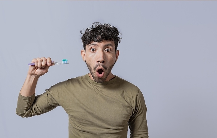 Surprised young man holding a toothbrush with toothpaste. Amazed young man holding toothbrush with toothpaste isolated, guy with wow expression holding toothbrush isolated on white