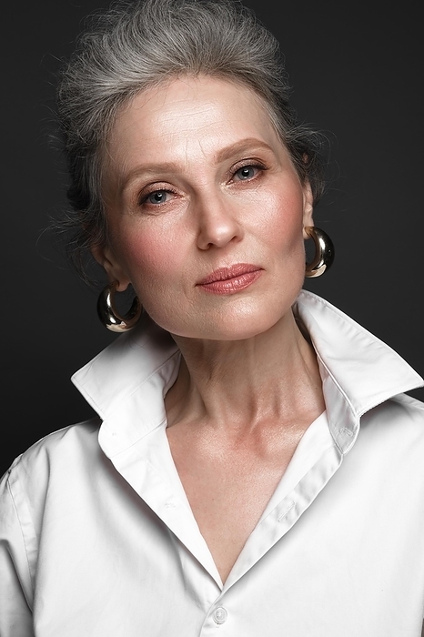Portrait of a beautiful elderly woman in a white shirt with classic makeup and gray hair