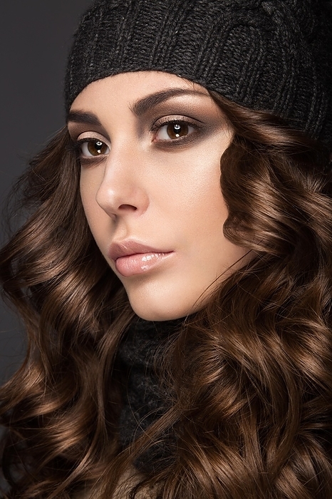 Beautiful girl with a Smokey make-up, curls in winter black knit cap. Warm winter image. Beauty face. Picture taken in the studio