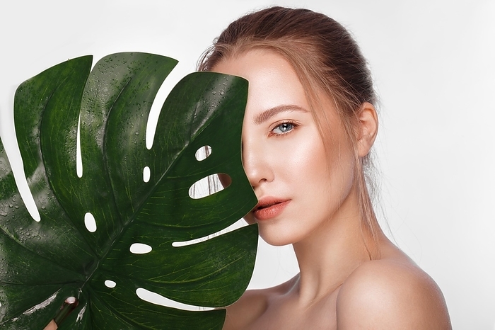 Beautiful fresh girl with perfect skin, natural make-up and green leaves. Beauty face. Photo taken in the studio
