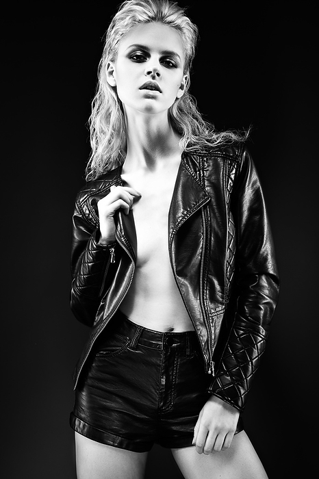 Daring girl model in black leather dress in the style of a rock on a naked body, dark makeup and wet hair. Picture taken in the studio. Black-and-white image