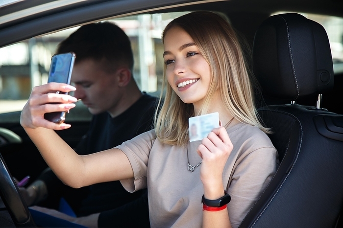 Happy smiling girl takes a selfie with a new drivers license, sitting next to an instructor