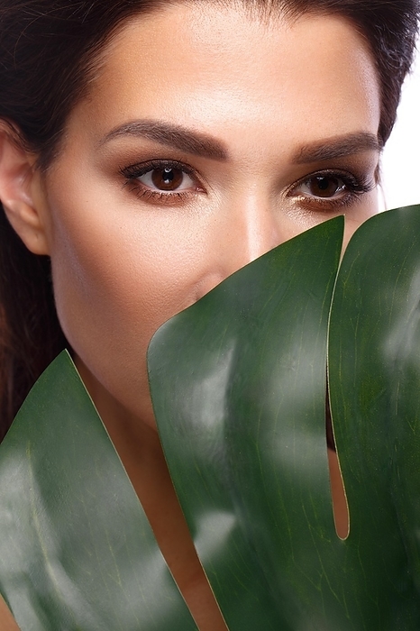 Beautiful fresh woman with perfect skin, natural make up and green leaves. Beauty face. Photo taken in the studio