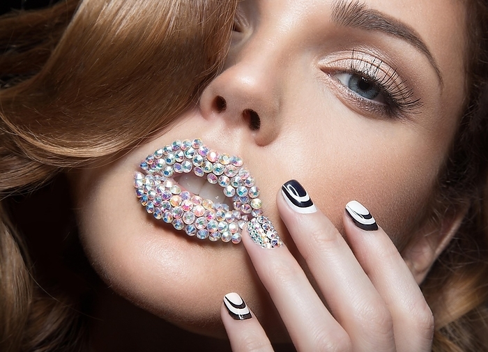 Beautiful girl with bright nails and lips of crystals, long eyelashes and curls. Beauty face. Picture taken in a studio