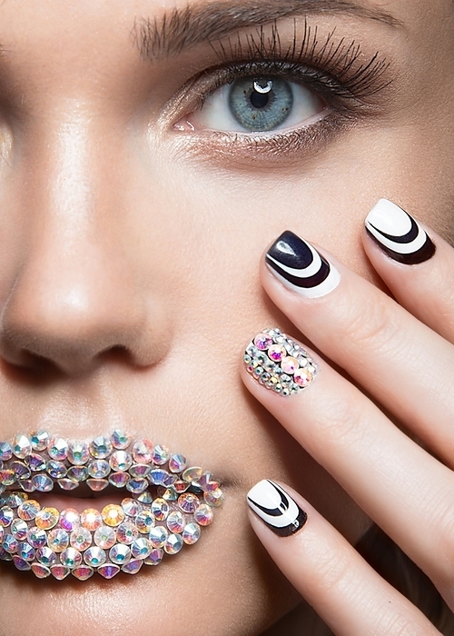 Beautiful girl with bright nails and lips of crystals, long eyelashes and curls. Beauty face. Picture taken in a studio