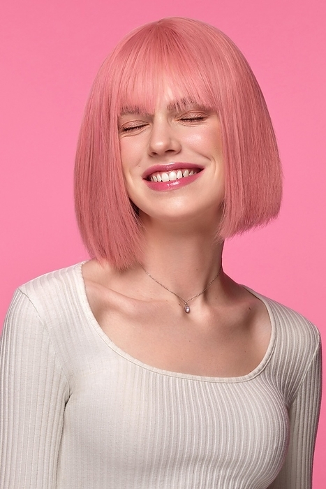 Beautiful funny cute woman in pink wig and classic makeup. The portrait was shot in a studio on a pink background. Beauty face