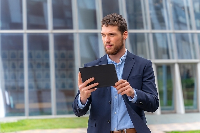 Young male businessman or entrepreneur outside the office, walking with a tablet in his hand