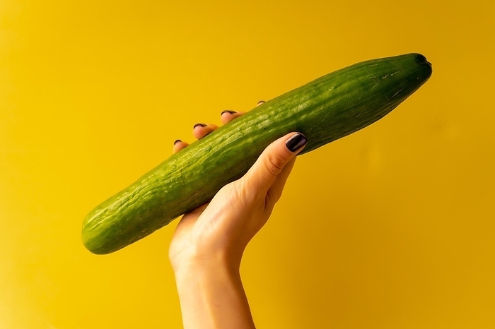 Woman's hand with a vegetable on a yellow background, healthy life, a Dutch cucumber