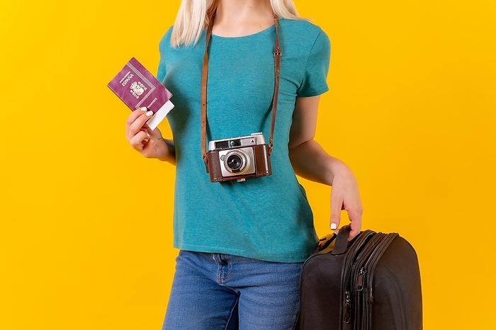 Unrecognizable person tourist with suitcase and passport, studio yellow background