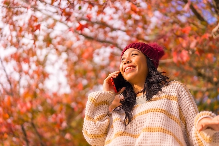 Portrait of an Asian woman in autumn with a mobile phone calling in a forest of red leaves, technology