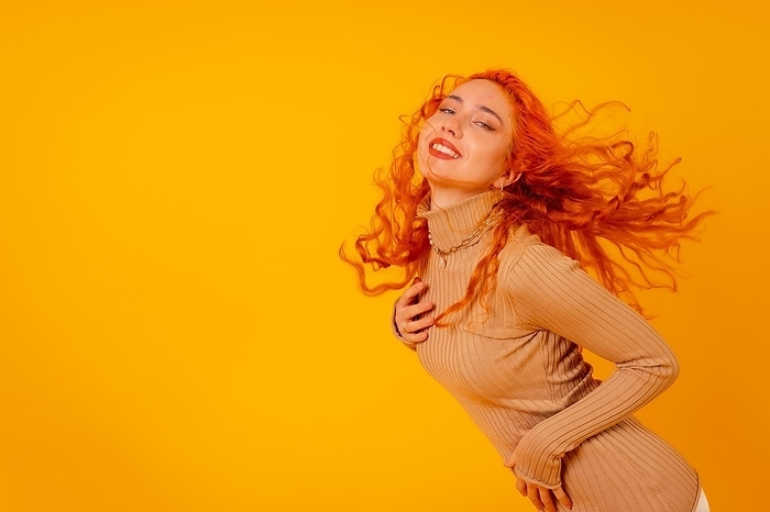 Red-haired woman on a yellow background, studio shot, moving her hair, tousled hair