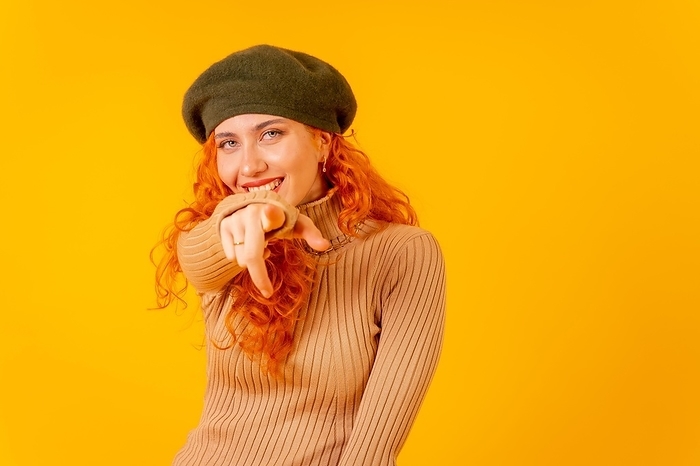 Red-haired woman in a beret in studio on a yellow background, copy space, throwing an ok