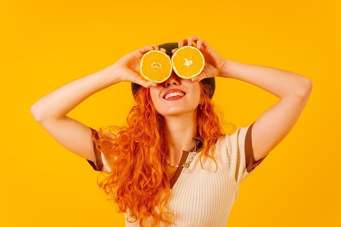 Redhead woman holding an orange over isolated yellow background covering eyes smiling