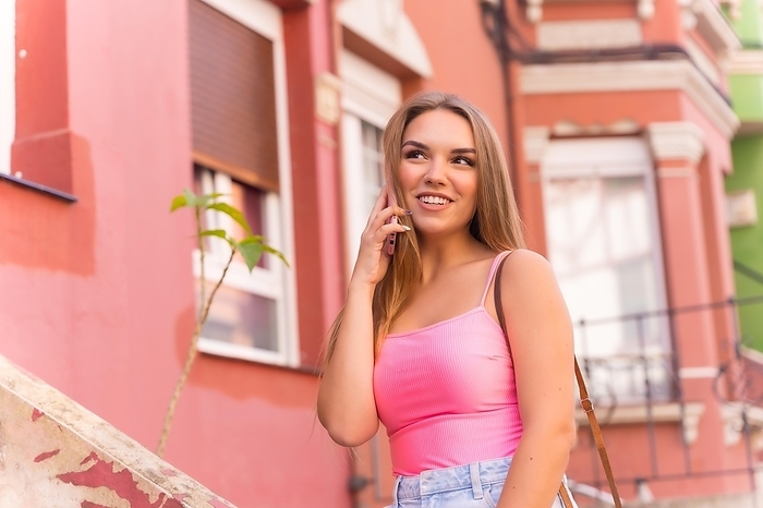 Young blonde caucasian tourist in a street with houses with colorful facades, talking on the phone