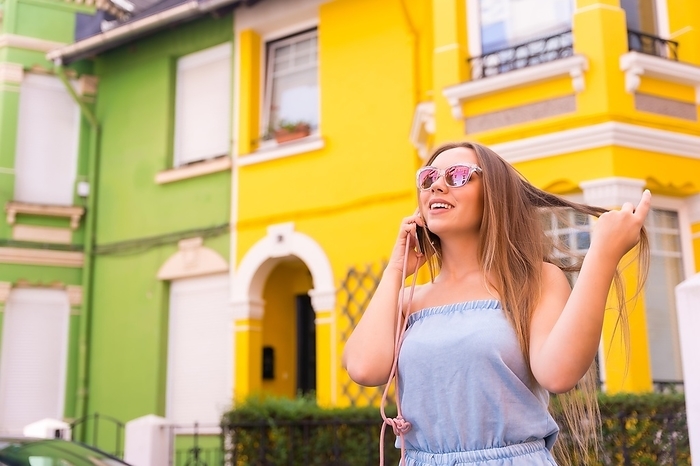 Portrait of young blonde tourist talking on the phone, behind yellow and green colorful facade