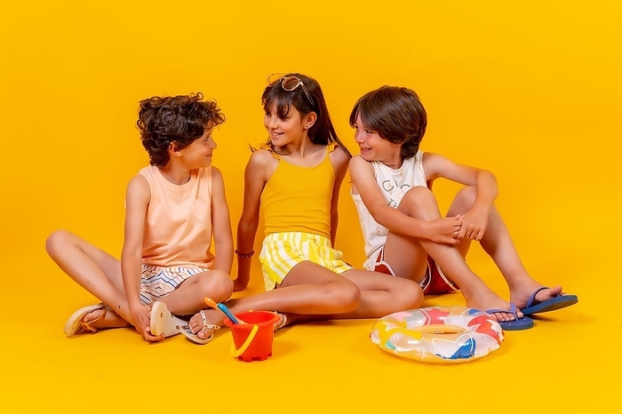 Portraits of children sitting on the floor enjoying holidays with toys, yellow background