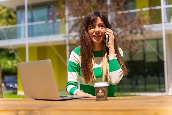 Portrait of a caucasian girl working with a computer in nature, talking on the phone
