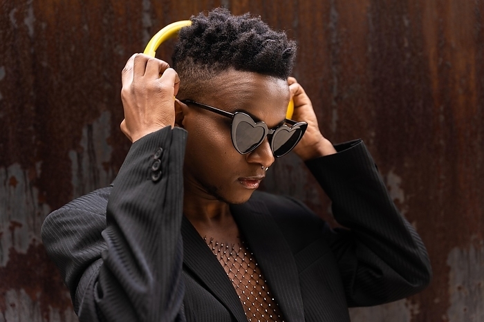 Black ethnic man listening to music wireless yellow headphones, wearing heart sunglasses, listening to modern music