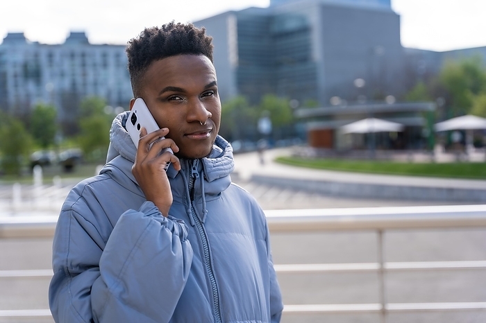 A black ethnic man with a phone and a blue jacket in the city, talking on the phone