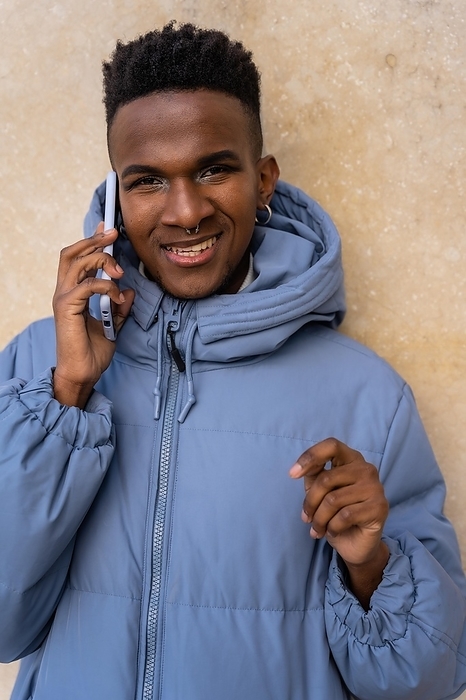 Portrait of a black ethnic man with a phone and a blue jacket on a yellow background, talking on the phone