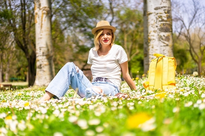 A young blonde girl enjoying spring in a park in the city, vacations next to nature and next to daisies