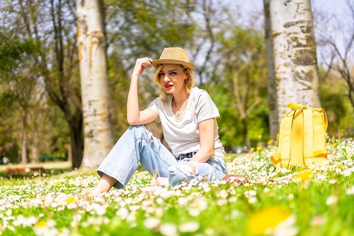 A young blonde girl in a hat enjoying spring in a park in the city, vacations next to nature and next to daisies
