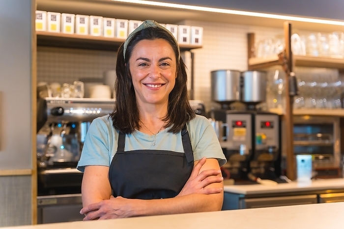 Portrait of a smiling waitress with the coffee machine in the background, the restrictions due to covid are lifted and the mandatory use of masks is removed