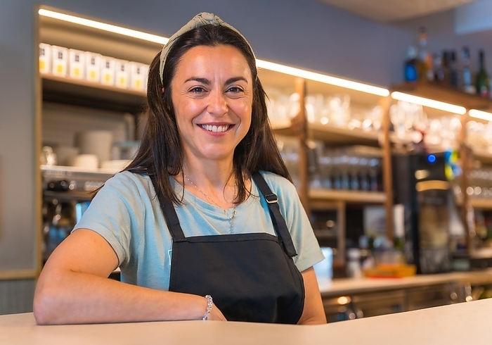 Portrait of a pretty smiling waitress with the coffee machine in the background, the covid restrictions are removed and the mandatory use of masks is removed