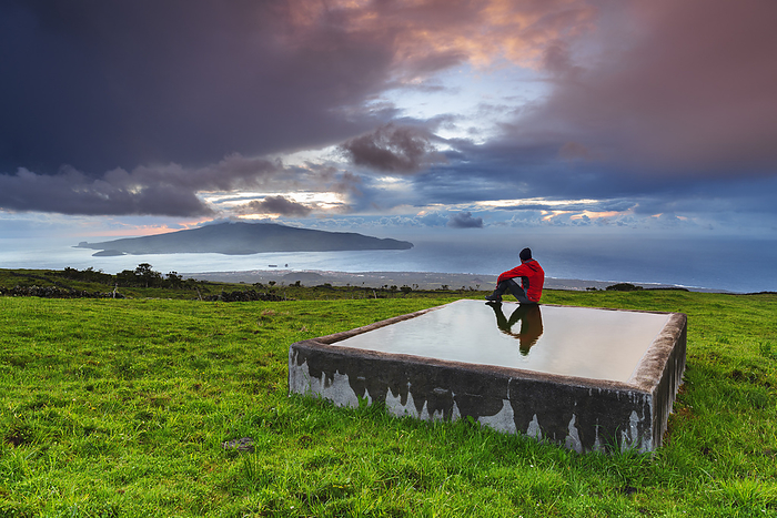 Portugal Man sits on the trough and admires the view of Faial island from Pico island at sunset, Madalena municipality, Pico island  Ilha do Pico , Azores archipelago, Portugal, Europe. Photo by: Paolo Graziosi