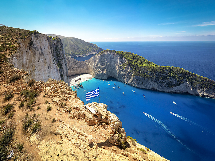 Zakynthos Island, Greece Greek flag on top of majestic cliffs, viewpoint of the famous Shipwreck Navagio Beach, Zakynthos, Greece. Photo by: Roberto Moiola