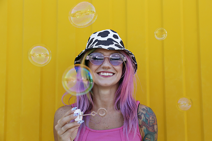 Happy woman holding bubble wand in front of yellow wall