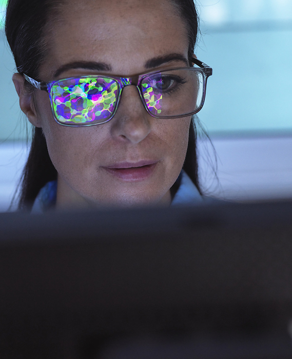 Scientist using computer with reflection of molecular structure on eyeglasses in laboratory