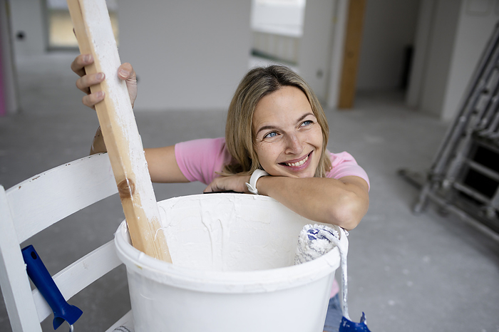 Happy woman day dreaming leaning on paint bucket in apartment