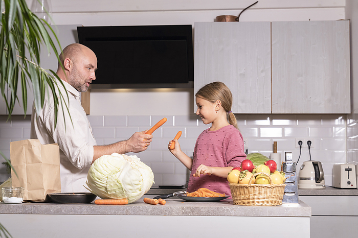 Father and daughter having fun with carrots in kitchen at home