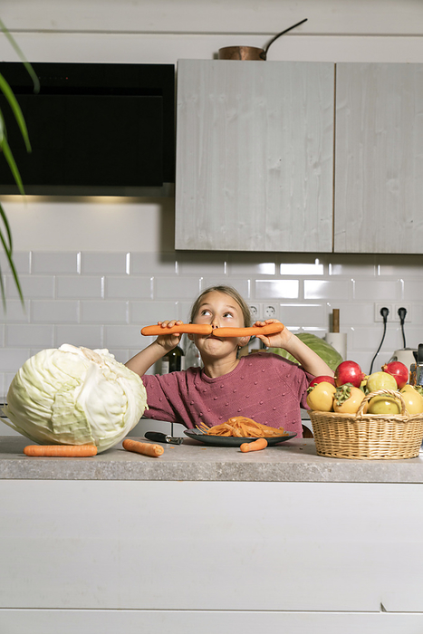 Playful girl having fun with carrots in kitchen at home
